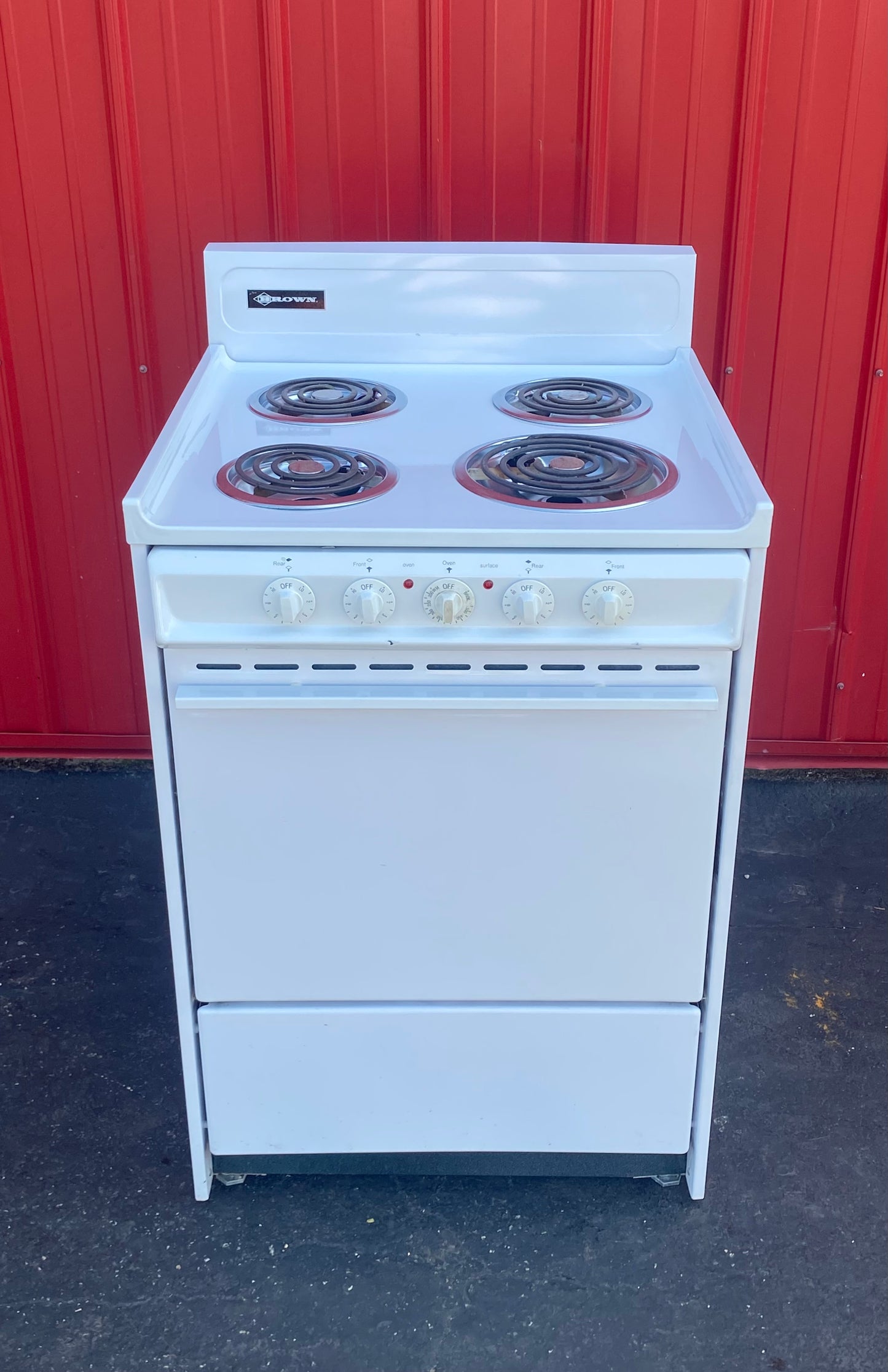 White electric stove against a red corrugated metal wall